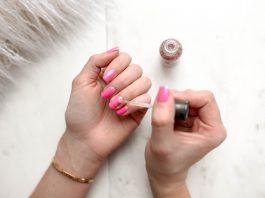 person spreading glittered nail polish on pink nails