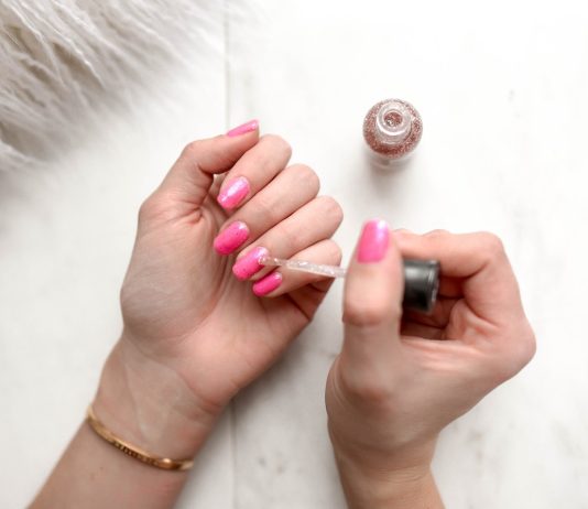 person spreading glittered nail polish on pink nails